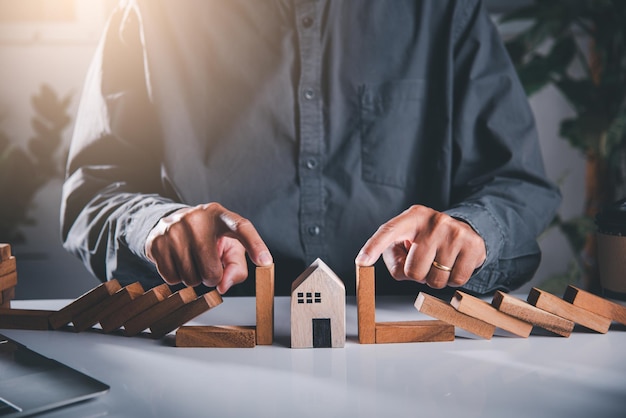 Man hand blocks wood block from many row falling wooden block like domino to house model