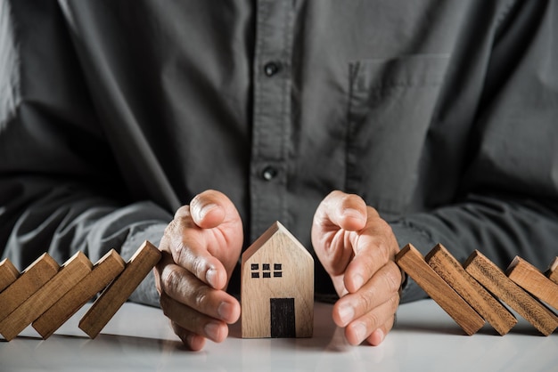 Man hand blocks wood block from many row falling wooden block like domino to house model