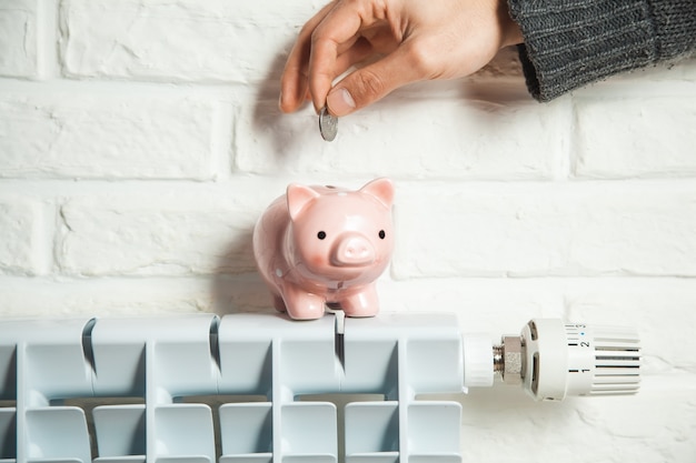 Man hand coin and piggy bank on heating system