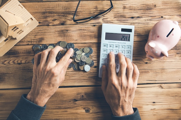 Man hand coins with calculator and house model on desk