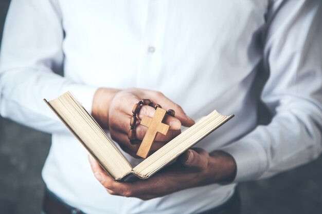 Man hand cross with book on dark background