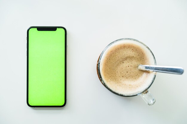 뜨거운 커피의 남자 손 컵과 녹색 화면 상위 뷰를 보고 스마트폰 사용