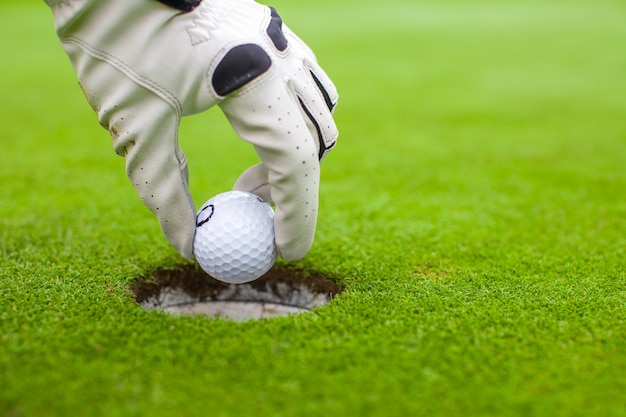 Man hand die een golfbal zet in gat op het groene gebied