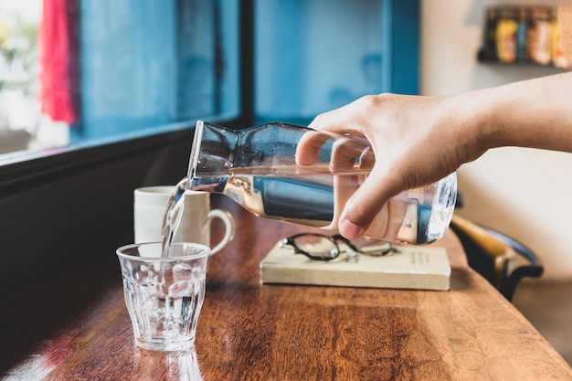 Man hand die zoet water van waterkruik gieten in een glas in koffie.