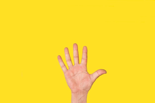 コピースペースで黄色の背景に5番目のジェスチャーをしている男の手