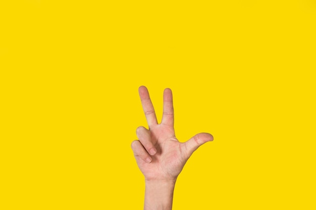 Man hand doing number three gesture on a yellow background with copy space