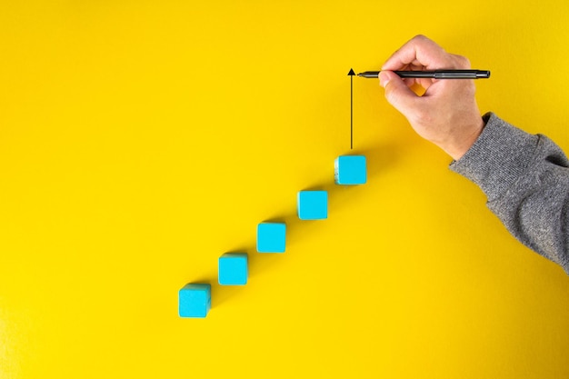 Man hand drawing an upward pointing arrow on top of growing graph made of wooden block