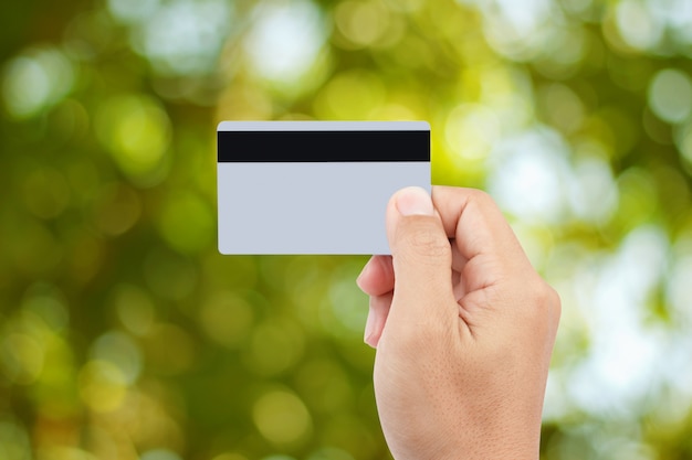 Man hand holding credit or debit card  on abstract green bokeh background