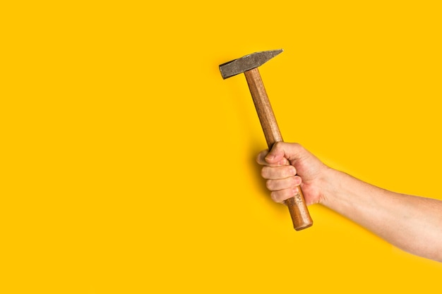 Photo man hand holding a hammer on a yellow background with copy space