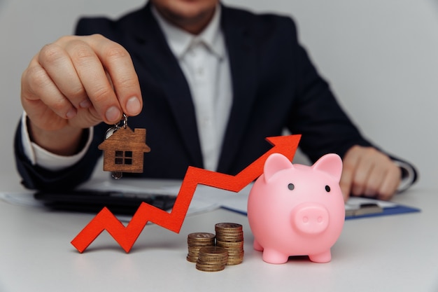 Man hand holding house key. Red arrow and stack of coins money. Business investment and real estate concept