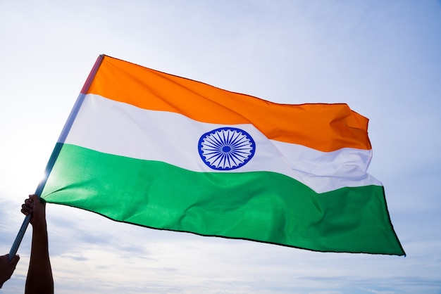Photo man hand holding india flag on the blue sky background.