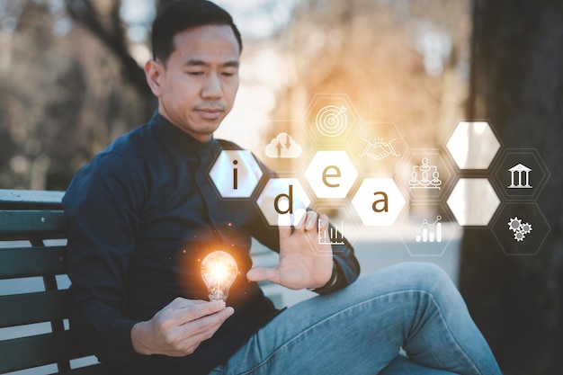 Мужчина держит в руках лампочку с линейным подключением и иконным бизнесом в парке Экономия идей и инвестиционного бюджета Креативная концепция идеи нового целевого бизнеса Работа вне дома