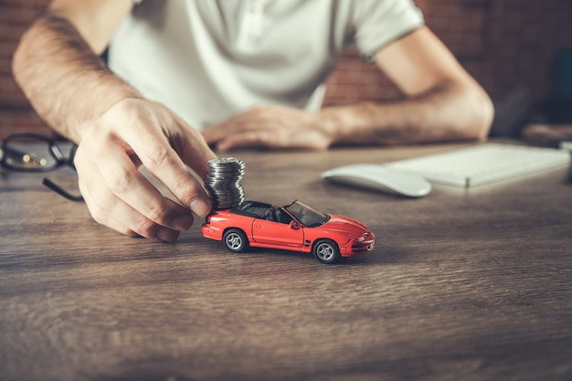 Man hand holding model of  car and coins