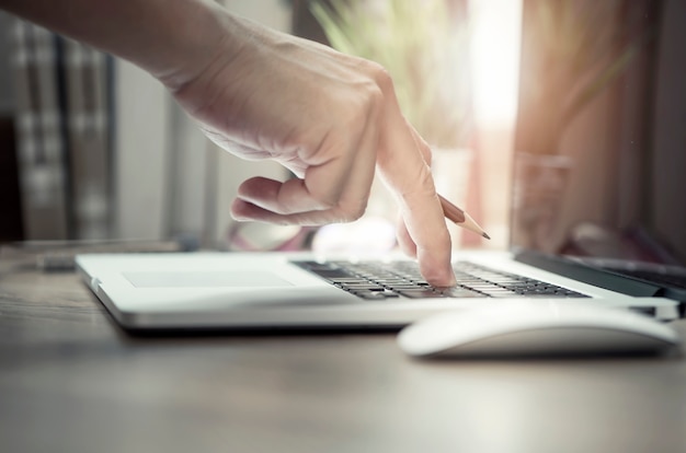 man hand holding pencil and typing on laptop keyboard