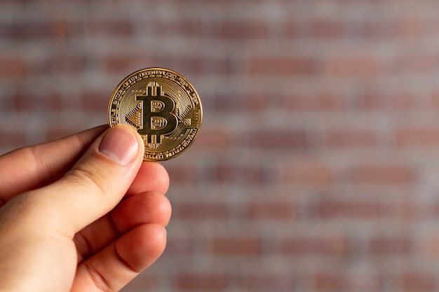 Man hand holding a physical bitcoin in front of a brick wall