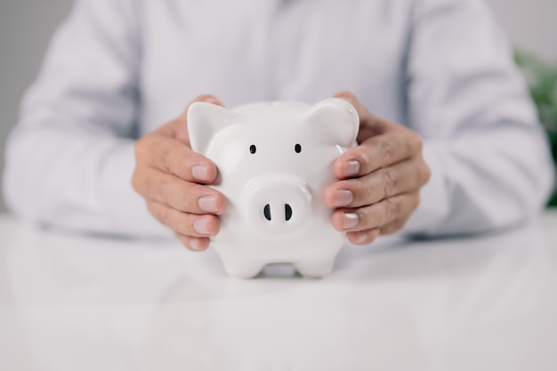 Man hand holding piggy bank on white table. Save money and financial investment