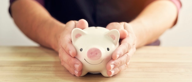 Man hand holding piggy bank on wood table. A saving money for future investment concept.