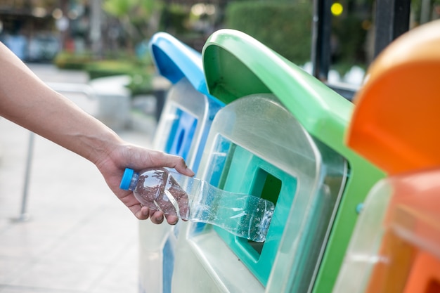 Equipaggi la mano che tiene e che mette lo spreco di plastica della bottiglia nei rifiuti dell'immondizia.