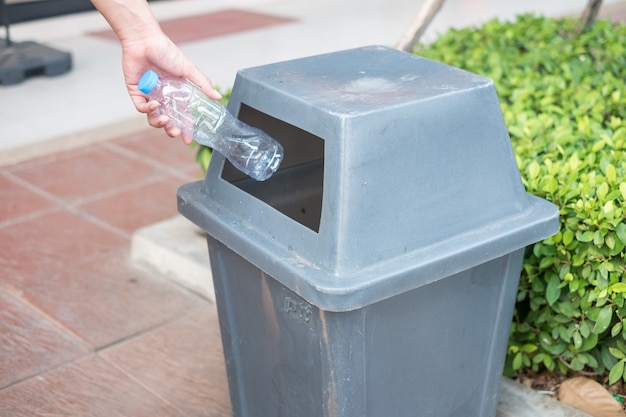 Equipaggi la mano che tiene e che mette lo spreco di plastica della bottiglia nei rifiuti dell'immondizia.