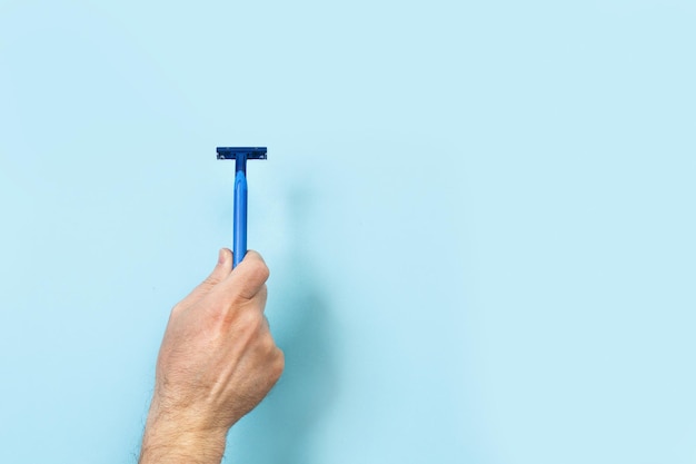 Man hand holding a razor on a blue  background with copy space