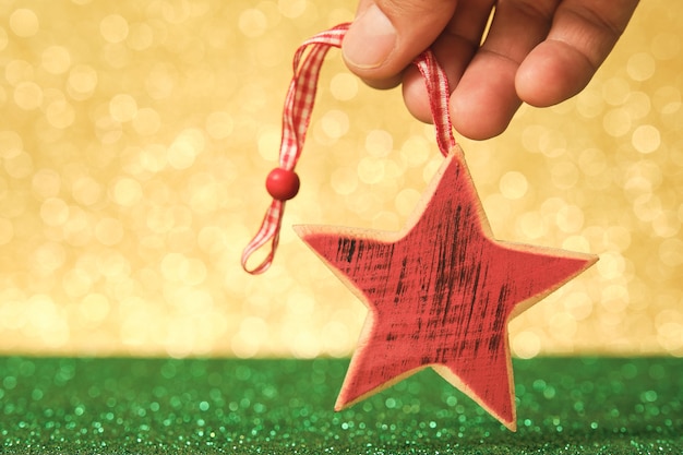 Man hand holding red star shaped christmas bauble on unfocused shiny green and gold background