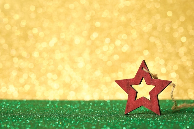 Man hand holding red star shaped christmas ornament on shiny green surface with unfocused shiny gold background