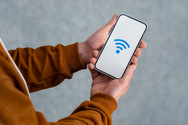 밝은 배경에 격리된 은색 스마트폰을 들고 있는 남자. 흰색 화면과 Wi-Fi 아이콘이 있는 전화 모형.