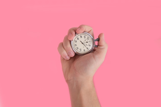 Man hand holding stopwatch on pink background.