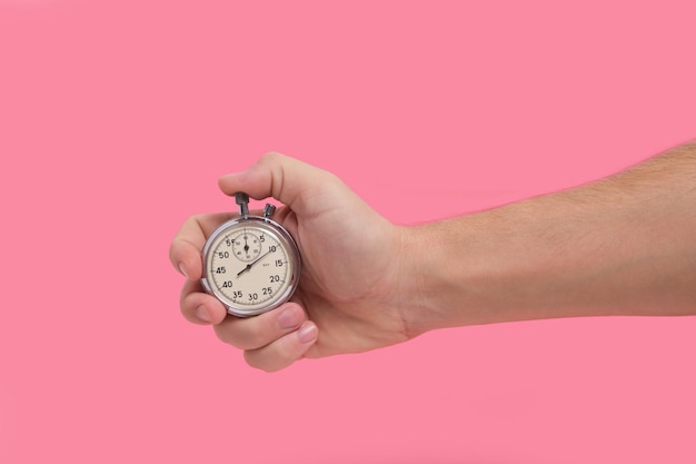 Man hand holding stopwatch on pink background.