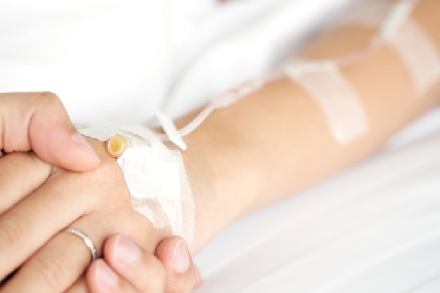 Man hand holding woman patient's hand on bed in hospital 