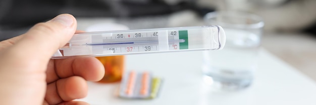 Man hand holds medical thermometer with temperature on background of sick woman lying on couh