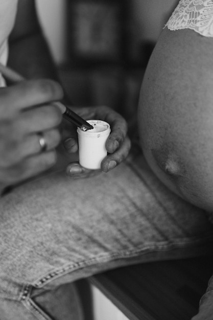 Фото Мужчина держит в руках краску и кисть, рисует желудок беременной женщины, черно-белое фото