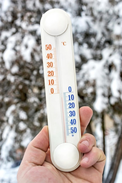 Man hand holds thermometer against trees in winter