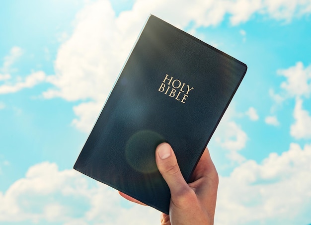 Man hand Holy Bible sky background