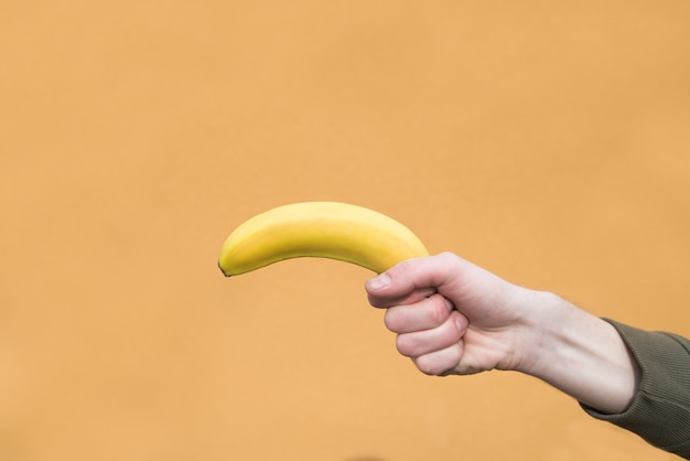 Man hand houdt een banaan op een oranje muur. Copyspace