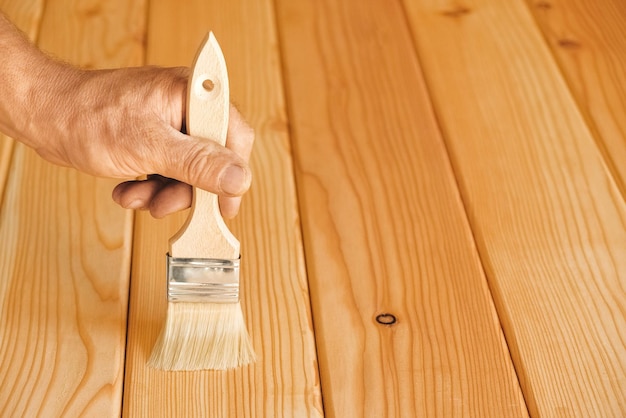 Man hand met een borstel op natuurlijke houten planken achtergrond