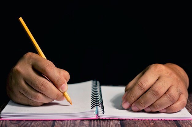 Man hand met geel potlood schrijven op notebook.