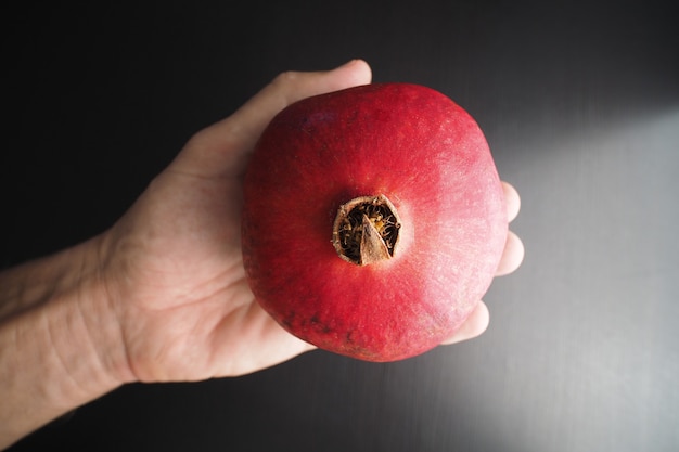 Foto man hand met rijpe granaatappel op donkere achtergrond.