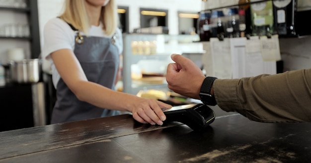 Man hand met smartwatch met terminal voor betaling, niet-contante transactie, zijaanzicht. Niet-contant betalingsconcept. Pos-terminal op tafel op zwarte achtergrond.