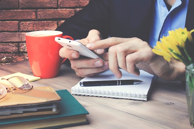 Man hand met telefoon met papieren notitieblok en kopje koffie op houten tafel