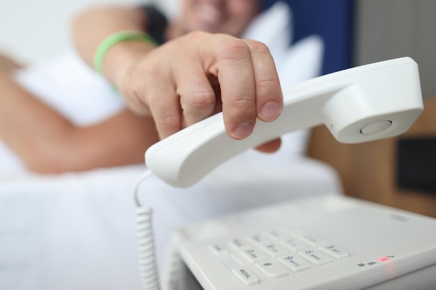 Foto mano dell'uomo che prende il ricevitore del telefono nel concetto di servizio in camera dell'hotel del primo piano della camera da letto