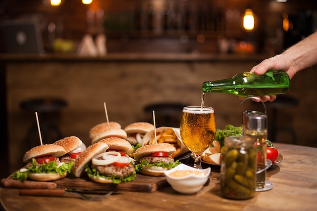 Photo man hand pours larger beer in a glass standing on a vintage table .blurred counter bar . jar of pickles.