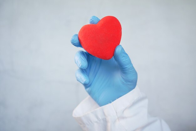 Mano dell'uomo in guanti protettivi che tengono cuore rosso su sfondo bianco