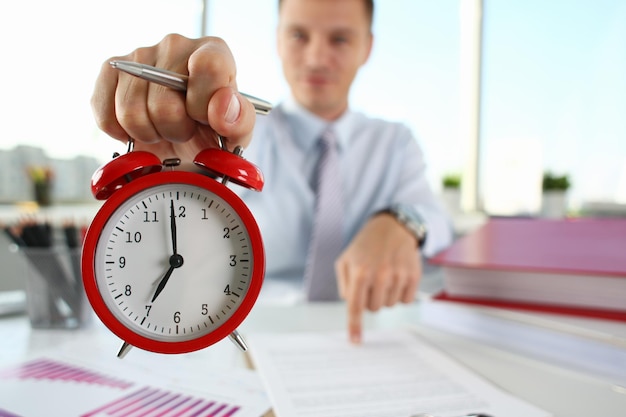 Man hand on red alarm clock stands at desk in office showing seven oclock am pm