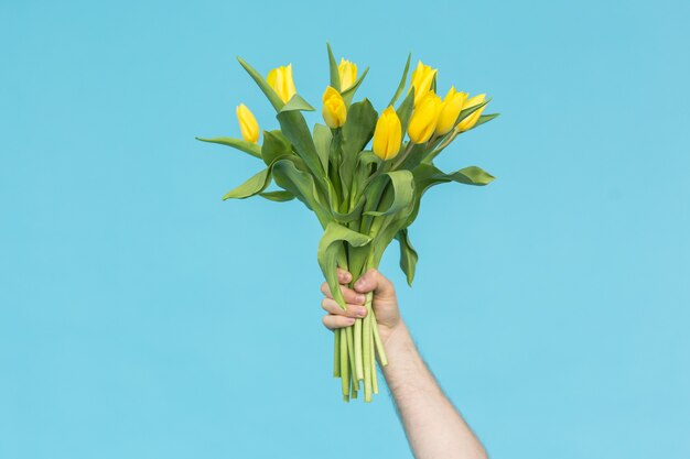 Man hand reiken een bos gele tulpen op blauwe muur