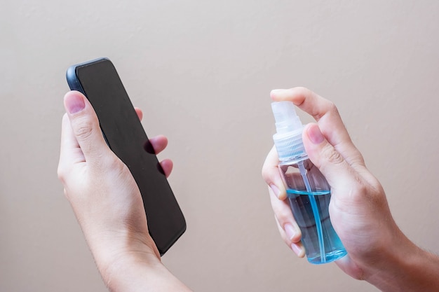 Man mano spruzzare alcol disinfettante bottiglia per lo smartphone