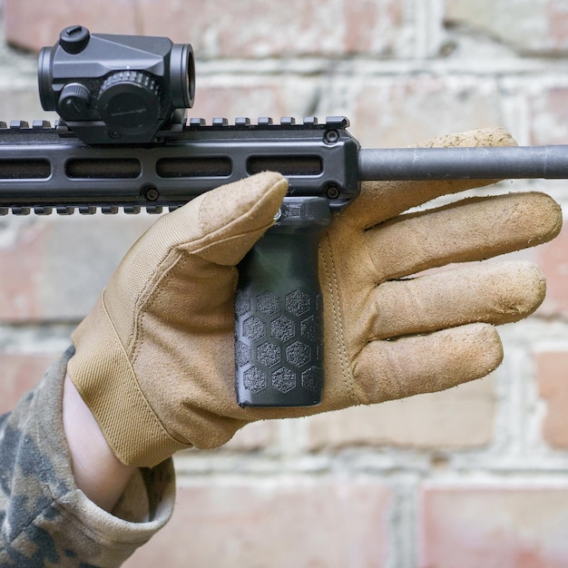 Mano dell'uomo nel guanto tattico tenere l'impugnatura anteriore per una pistola da tiro pistola im mano dell'uomo pronta per l'uso tiratore pronto a colpire il bersaglio con una presa della mano