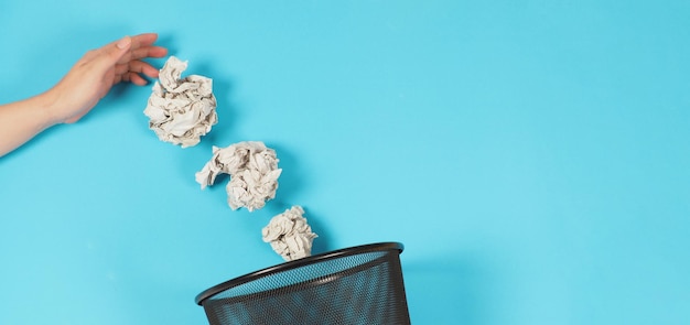 Man hand and three crumpled white paper and a bin on blue background