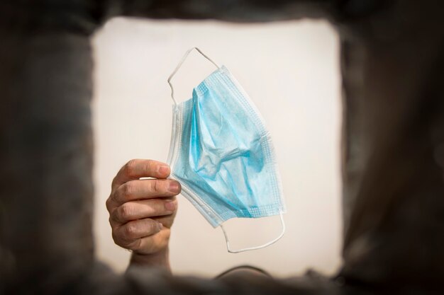 Man hand throws protective medical or surgical mask into the trash outdoors. Protection against influenza and the viral ncov epidemic, quarantine, concept image.