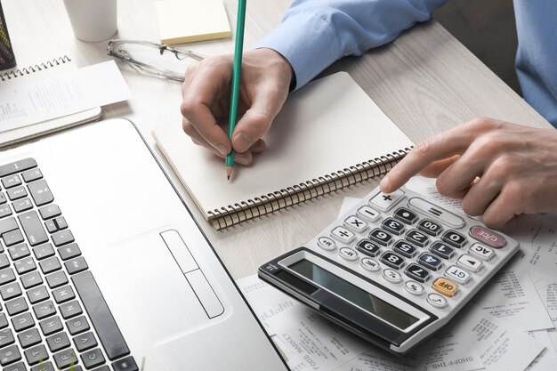 Man hand using calculator and writing make note with calculate about cost and taxes at home office. Businessman doing some paperwork in the workplace